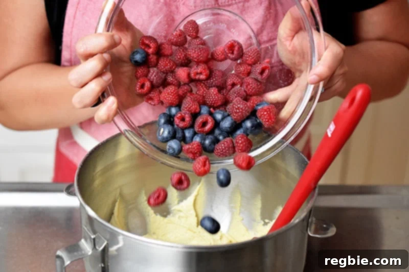 Adding blueberries and raspberries to a mixing bowl to make paleo berry snack cake.