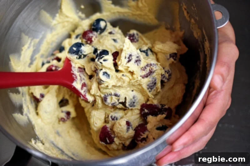 A red silicone spatula is folding in the berries in the berry snack cake batter.