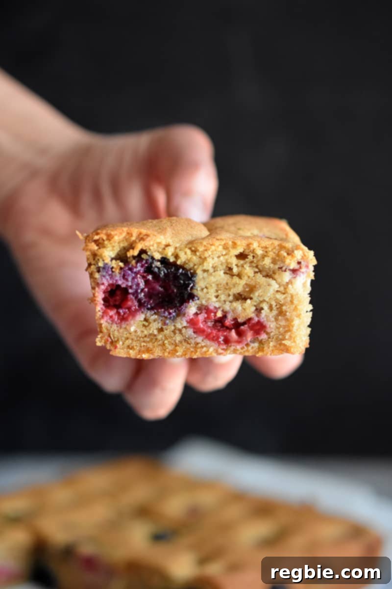 Someone holding a square slice of paleo and gluten-free berry snack cake.