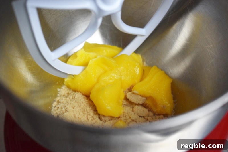 A stand mixer bowl has ghee and maple sugar in it, along with the paddle attachment.