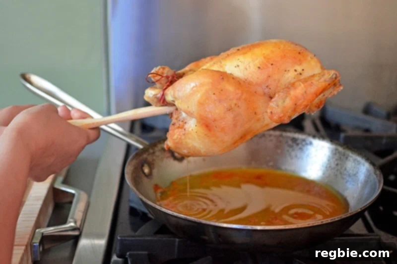 Using a spatula to gently guide the flavorful pan drippings from a Weeknight Roast Chicken back into the skillet, preserving all the delicious juices.