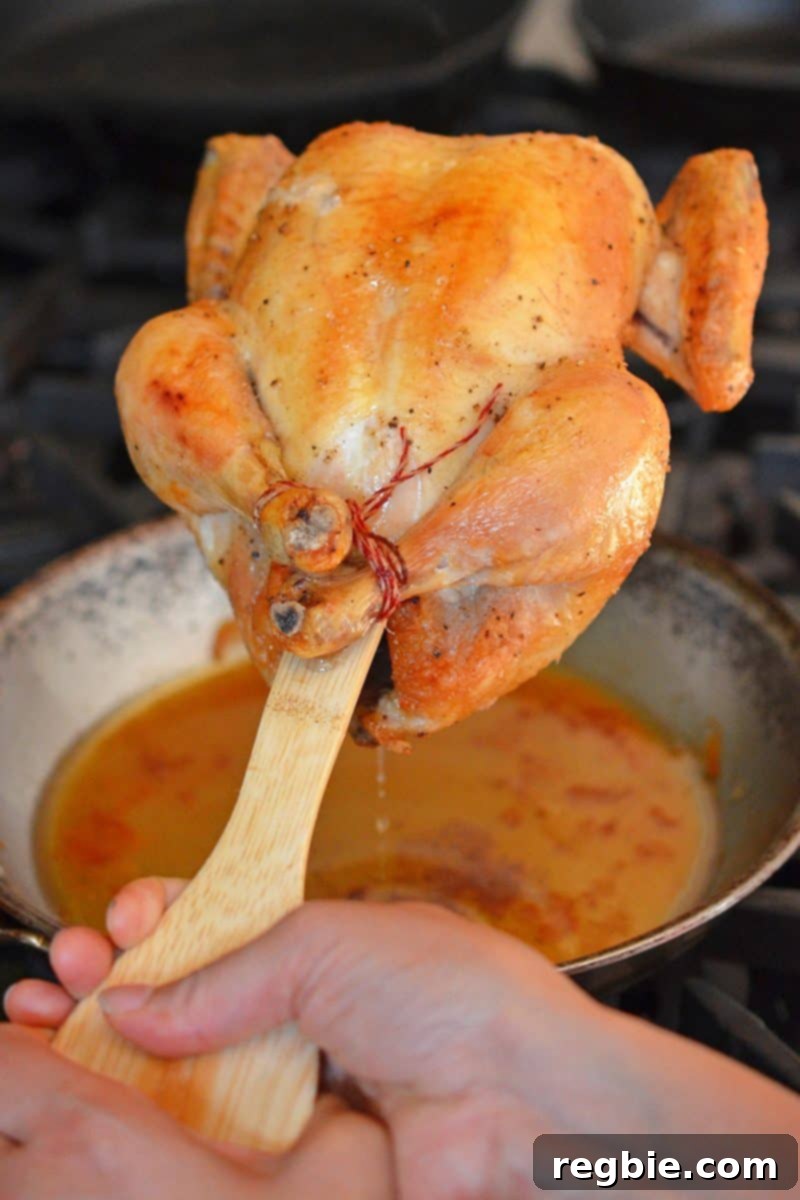The handle of a wooden spatula skillfully positioned to assist in draining delicious juices from a perfectly roasted Weeknight Roast Chicken into a frying pan below.