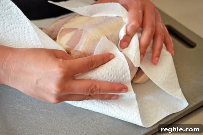 Someone meticulously patting dry a raw whole chicken with paper towels, a crucial step for achieving crispy skin in this simple roast chicken recipe.