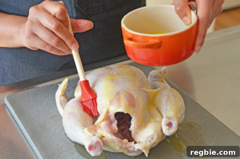 Brushing melted ghee evenly over a raw whole chicken resting on a gray cutting board, preparing it for a healthy and delicious weeknight roast.