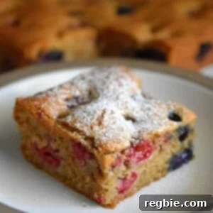 A slice of paleo and gluten-free berry snack cake is on a white plate. In the background are the other slices of berry snack cake.