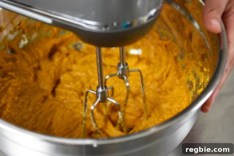 An overhead view of a hand mixer effectively combining the dry and wet ingredients into a smooth batter for paleo chocolate chip muffins.