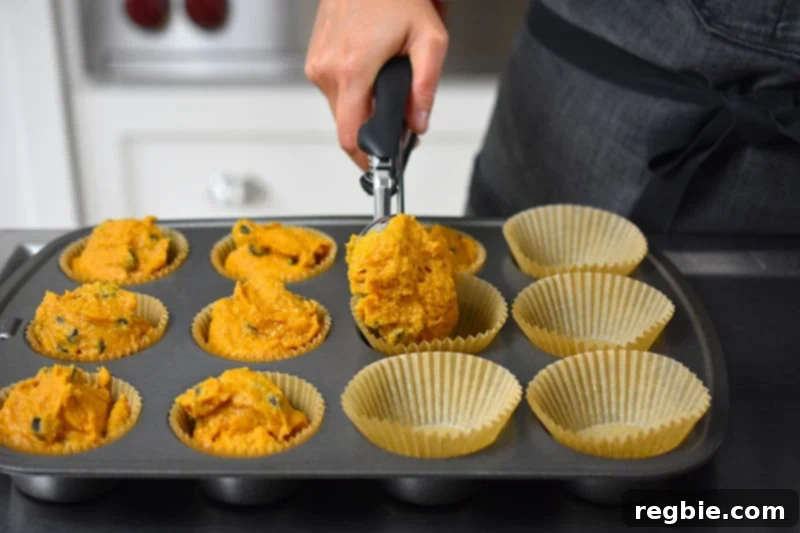 Using a large ice cream scoop to precisely divide the pumpkin chocolate chip muffin batter into each liner in the muffin tin.