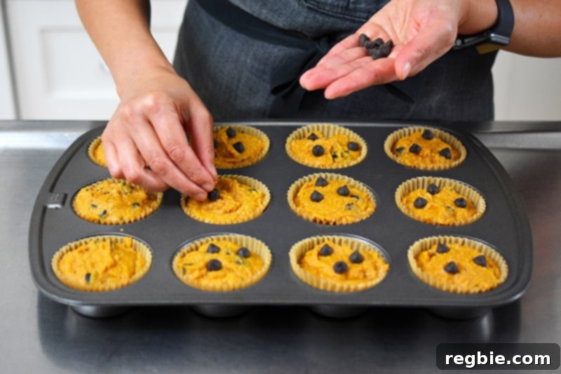 Sprinkling additional chocolate chips on top of the pumpkin chocolate chip muffins before baking them, enhancing their appeal.