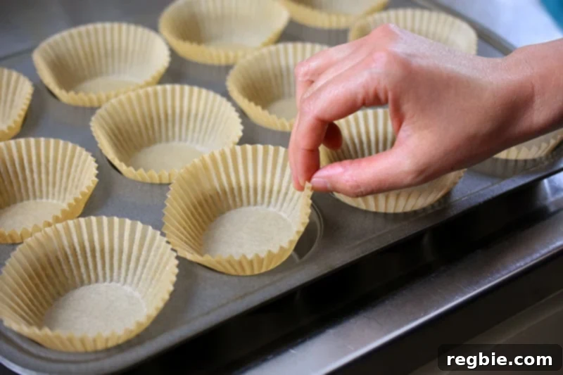 A hand placing parchment paper liners into a muffin tin, preparing it for baking paleo pumpkin chocolate chip muffins.