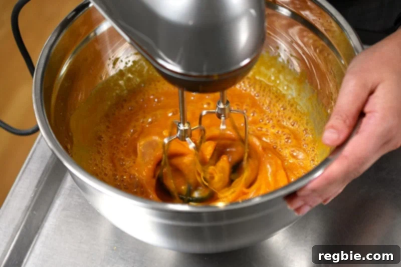 A hand mixer smoothly blending the wet ingredients—pumpkin purée, honey, eggs, and vanilla—for a delicious batch of paleo and gluten-free pumpkin chocolate chip muffins.