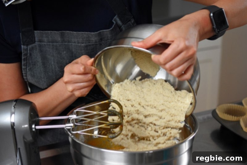 Carefully adding the bowl of prepared dry ingredients to the mixed wet ingredients, initiating the quick combination for the pumpkin chocolate chip muffin batter.