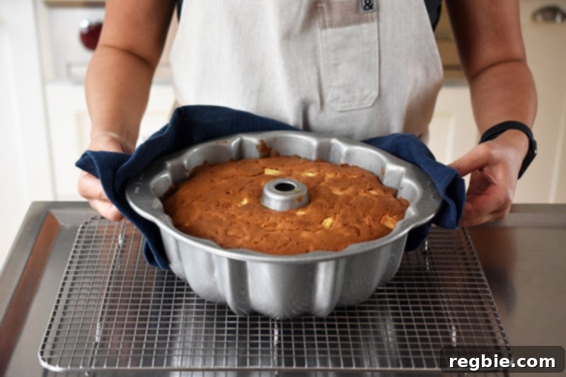 Grain Free Spiced Apple Bundt Cake 16 Someone using an oven mitt to carefully place a freshly baked apple Bundt Cake, still in its pan, onto a wire rack to cool.