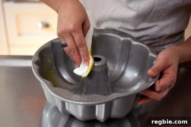 Grain Free Spiced Apple Bundt Cake 5 Someone meticulously using a paper towel to grease a 10-inch bundt pan with ghee, preparing it for the Paleo Apple Bundt Cake batter.