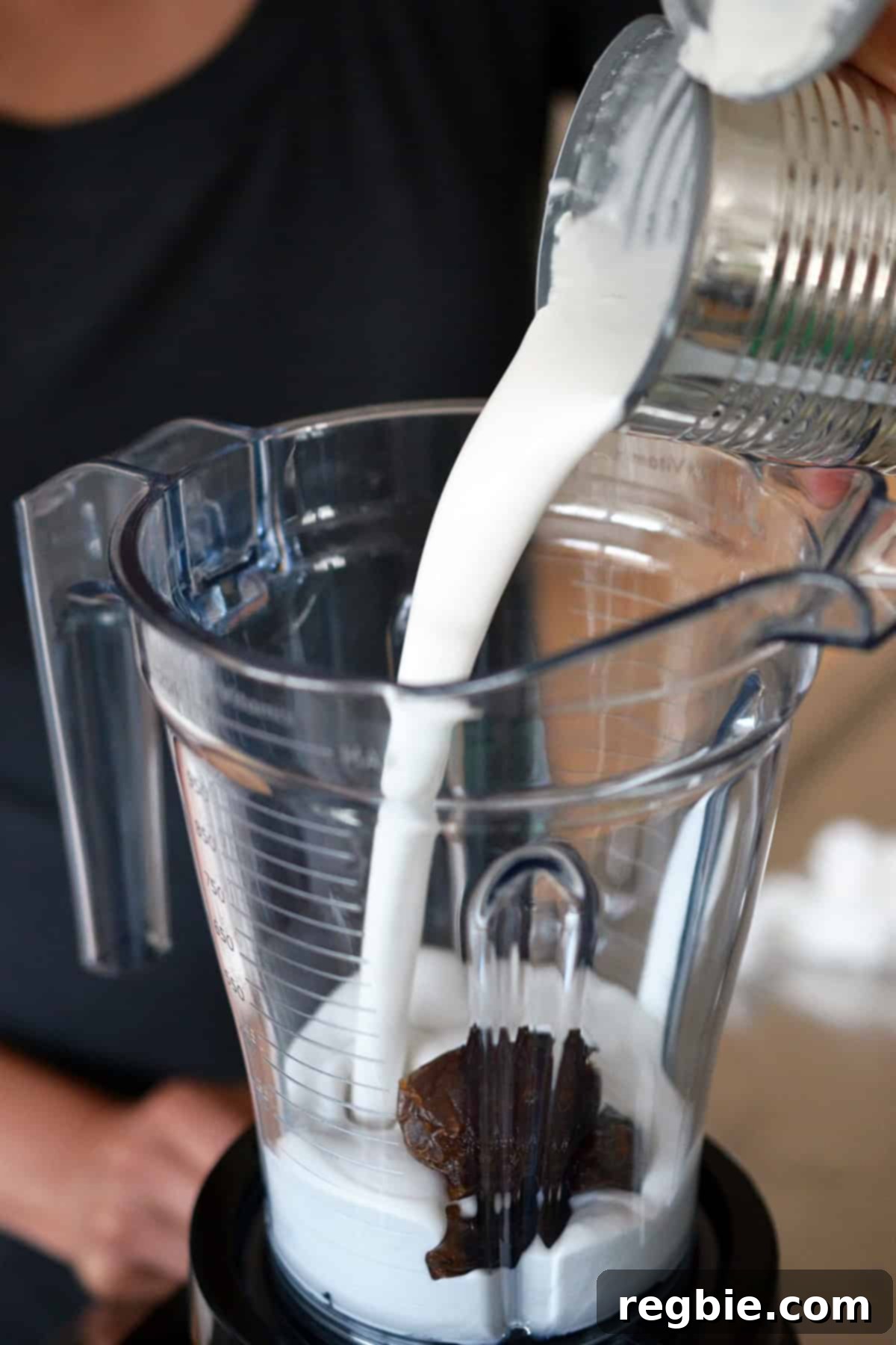 Pouring canned full-fat coconut milk into a blender containing pitted Medjool dates.