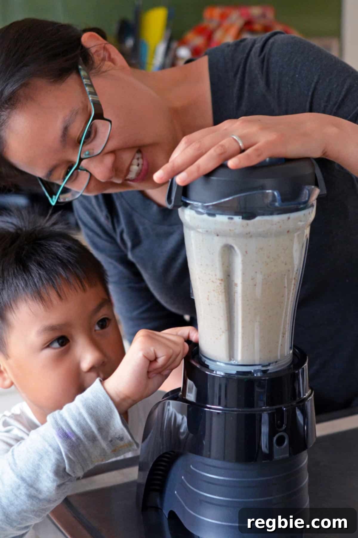 An Asian woman in glasses blending dairy-free ice cream batter in a blender, with a young Asian boy observing curiously.