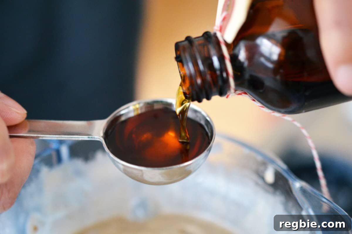 Pouring vanilla extract into a measuring spoon, ensuring precise flavoring for the ice cream.