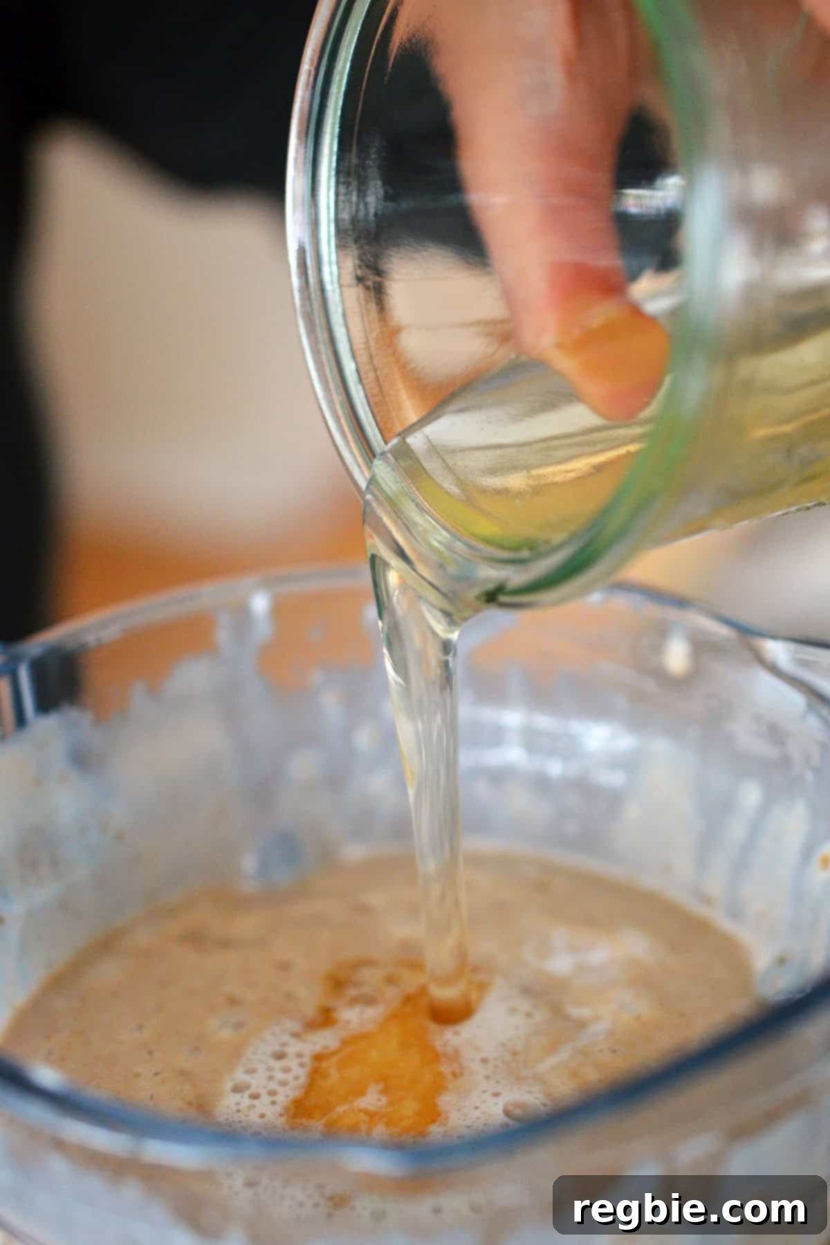 Pouring bloomed gelatin mixture into a blender filled with dairy-free ice cream batter, enhancing its texture.