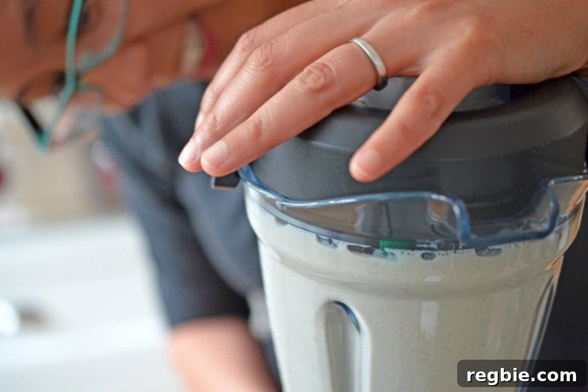 An Asian woman resting her hand on the lid of a blender, which contains a smooth dairy-free ice cream mixture.