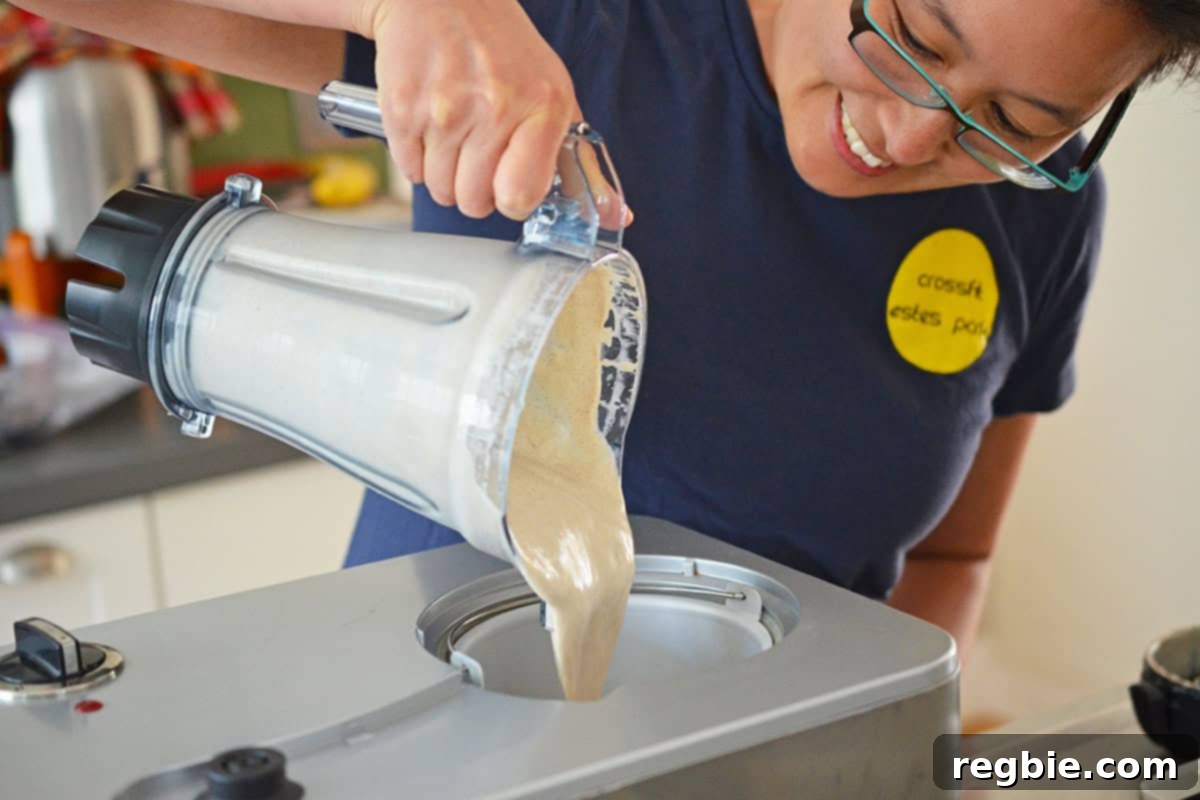 A smiling Asian woman pouring dairy-free vanilla ice cream batter from a blender into an ice cream maker, ready to churn.