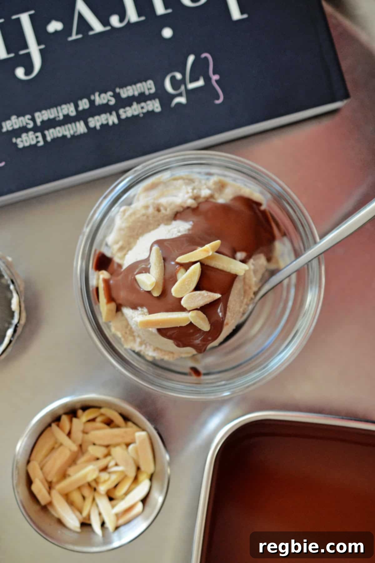 An overhead shot of a generous scoop of homemade dairy-free vanilla ice cream, beautifully adorned with chocolate ganache and crunchy almond slivers.