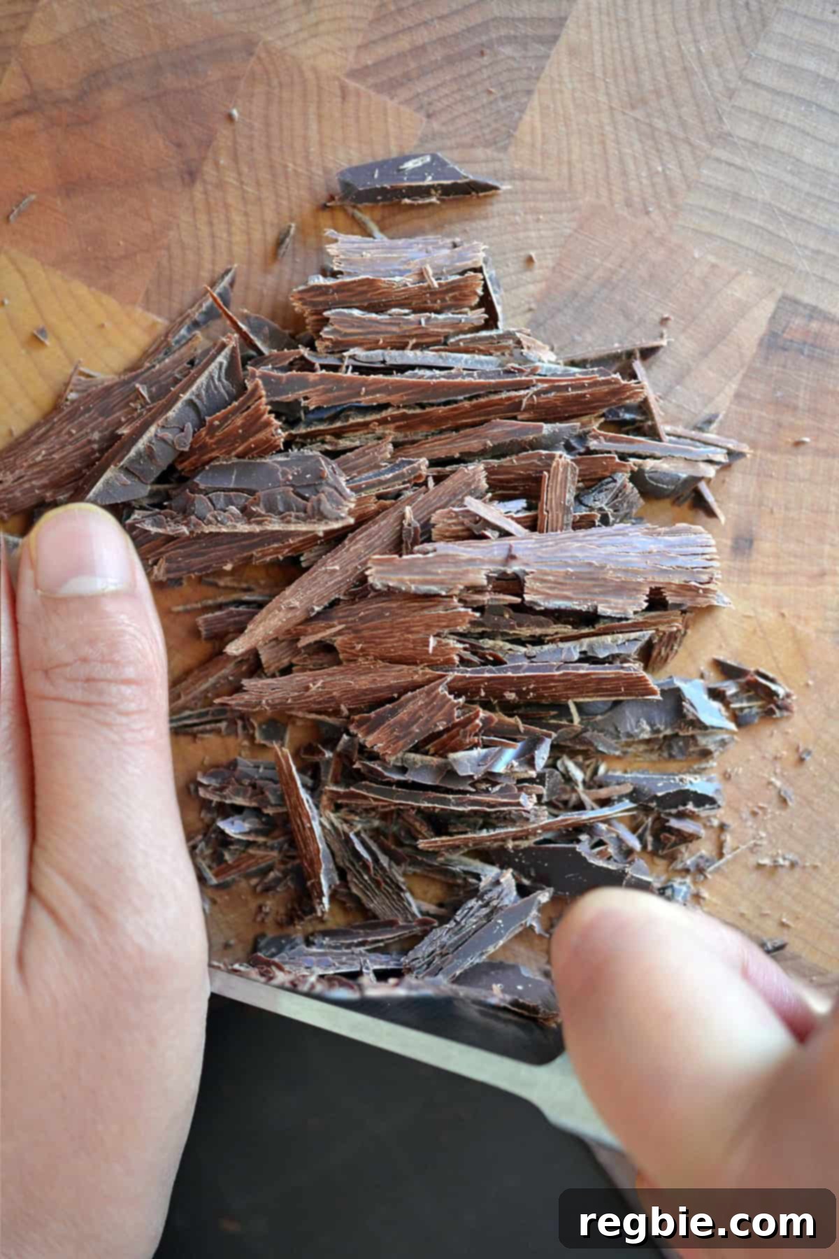 Finely chopped dairy-free dark chocolate neatly arranged on a wooden cutting board, ready for ganache preparation.