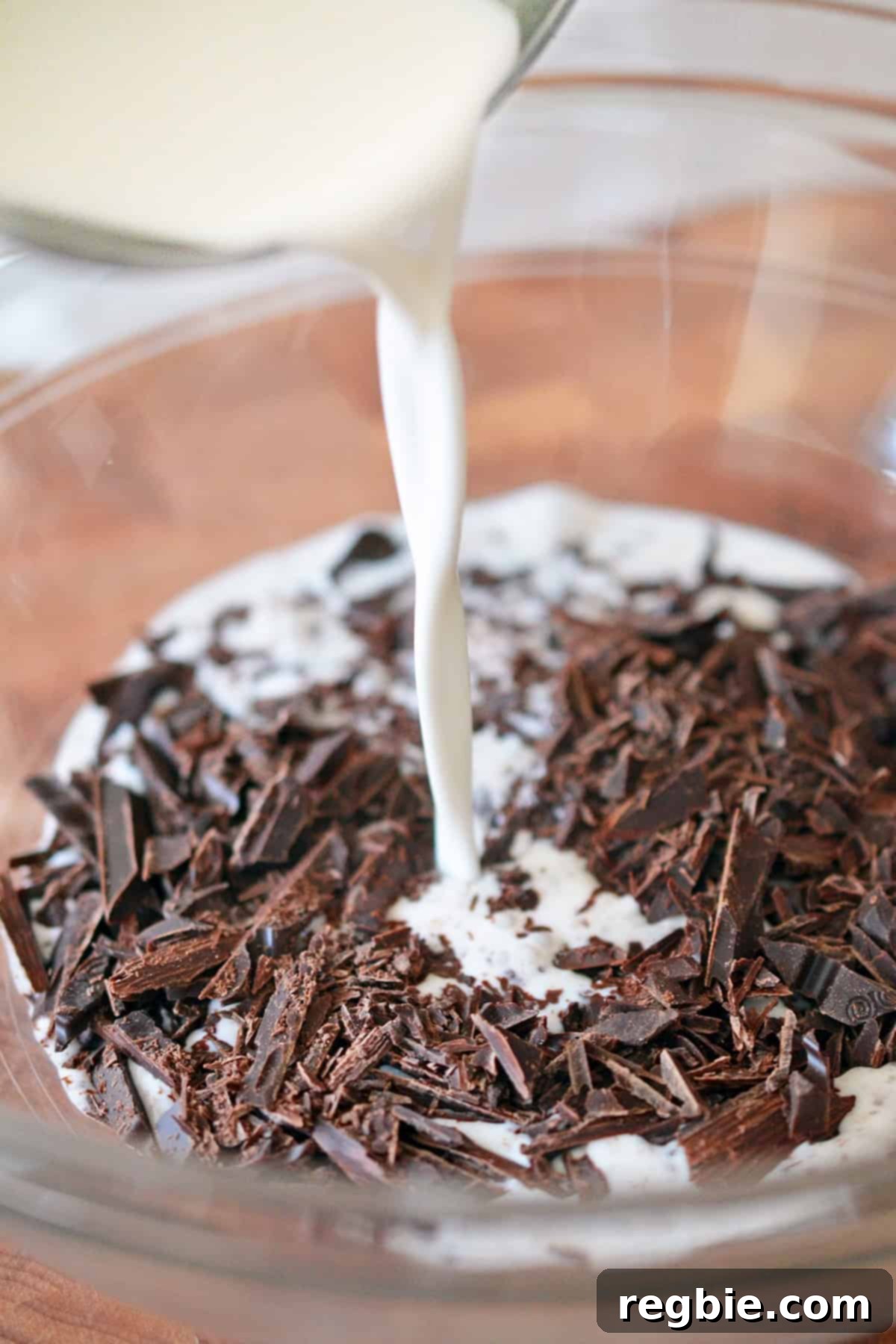 Pouring hot coconut milk over finely shaved dairy-free dark chocolate in a glass mixing bowl to initiate the ganache making process.