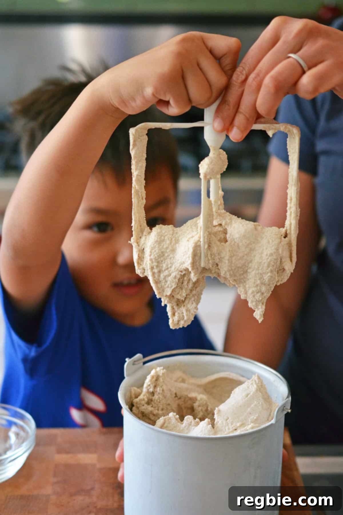 A young Asian boy helping his mom gently pull the plastic paddle out of an ice cream maker after the churning process is complete.