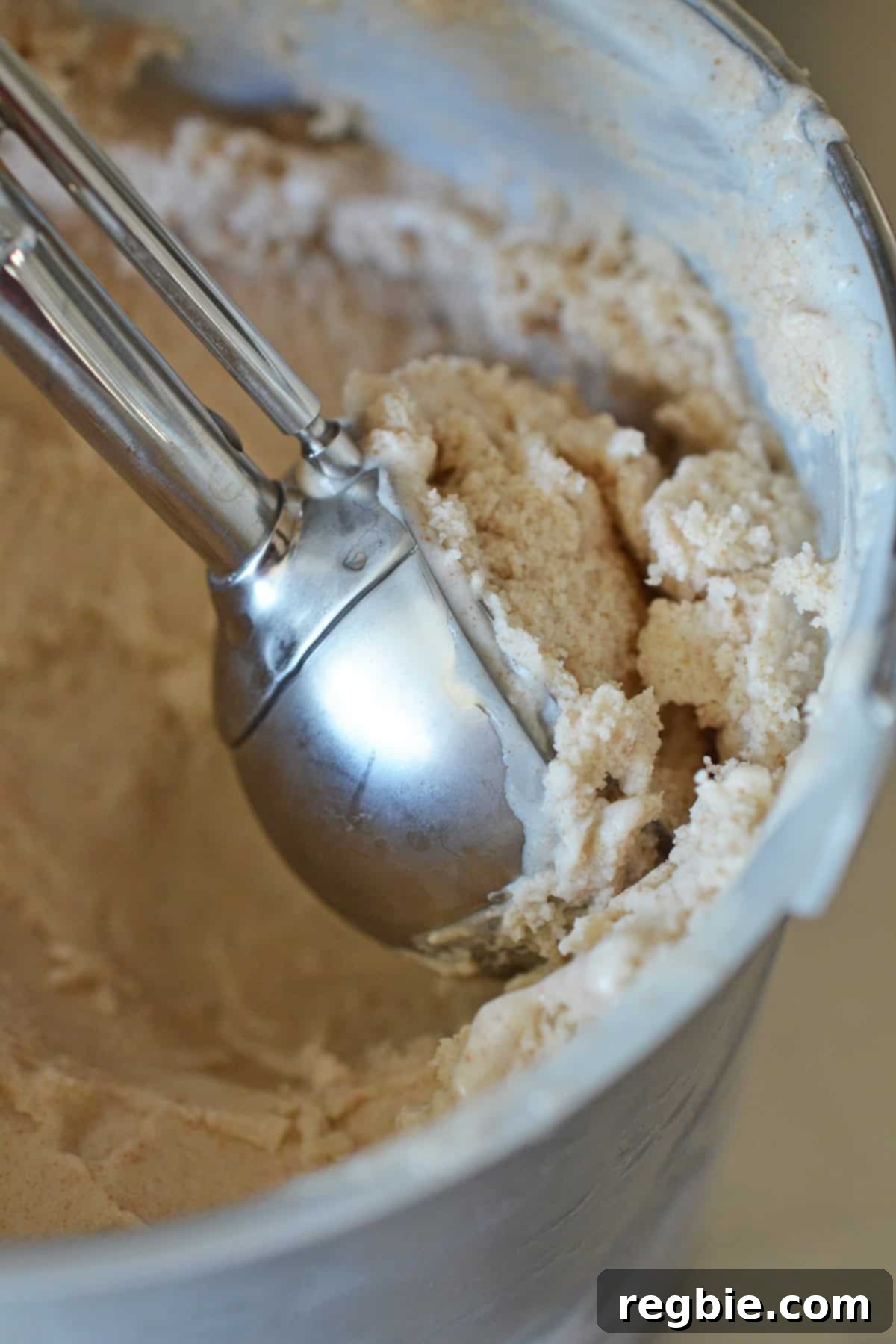 A close-up of a metal ice cream scooper effortlessly scooping creamy homemade dairy-free vanilla ice cream.