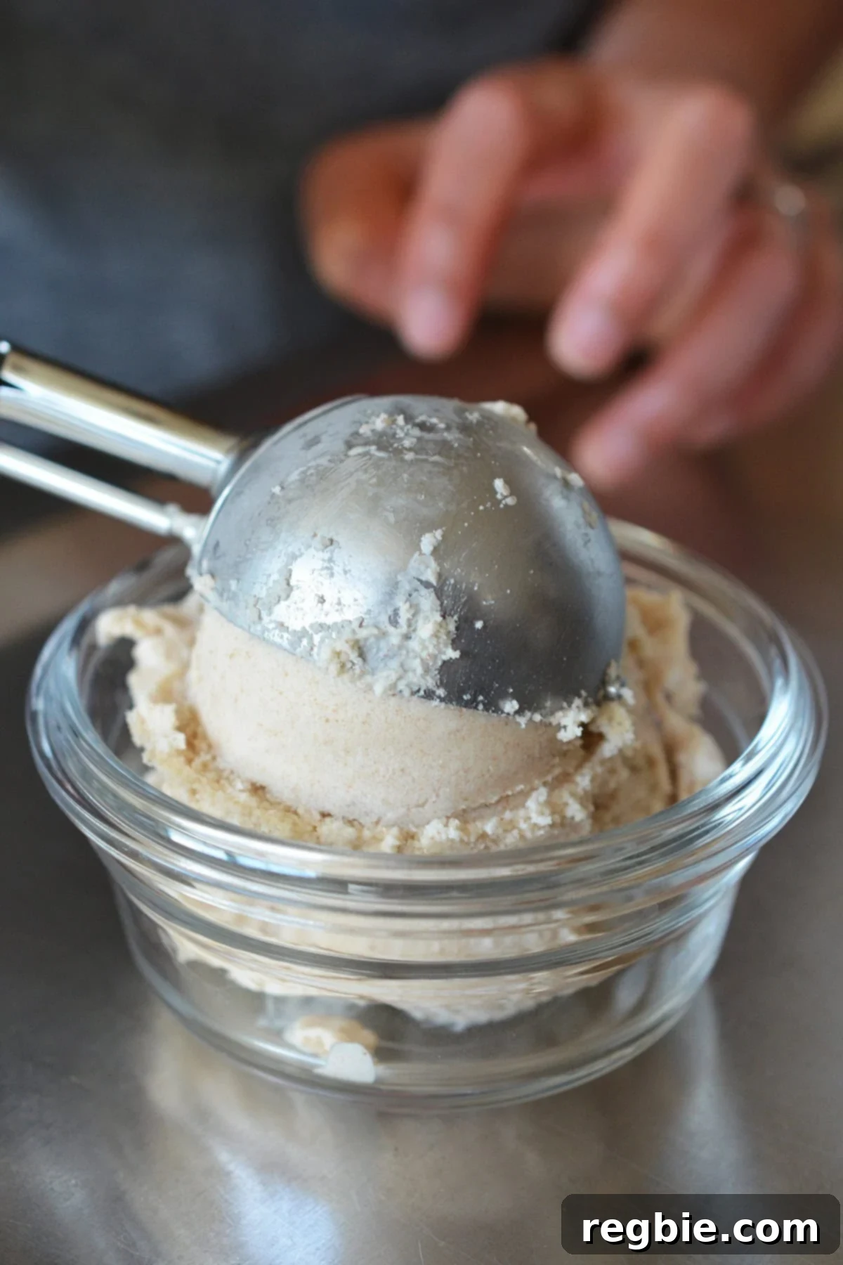 A metal ice cream scooper placing a perfect scoop of dairy-free vanilla ice cream into a small glass bowl.