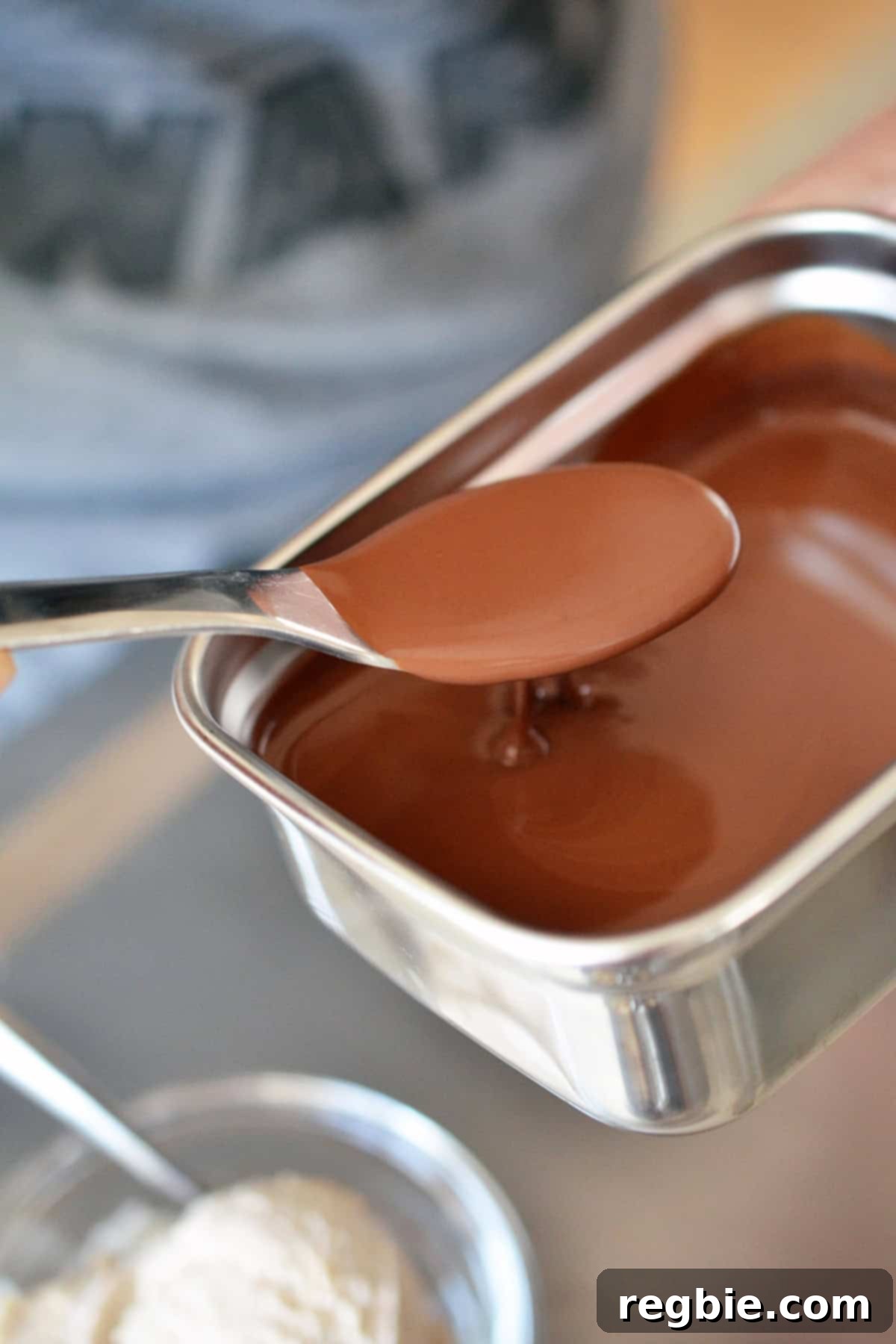 A spoon lifting a stream of rich chocolate ganache, poised to be drizzled over a scoop of homemade paleo ice cream.