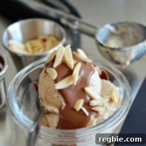 A side view of a scoop of homemade dairy-free vanilla ice cream topped with chocolate ganache and almond slivers, ready to be served.