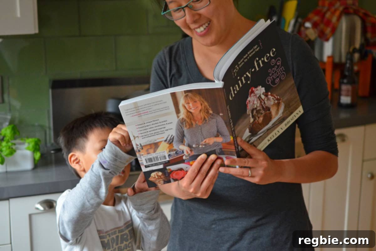 A smiling Asian mother showing a young Asian boy a recipe in a dairy-free ice cream cookbook, sharing a moment of culinary bonding.