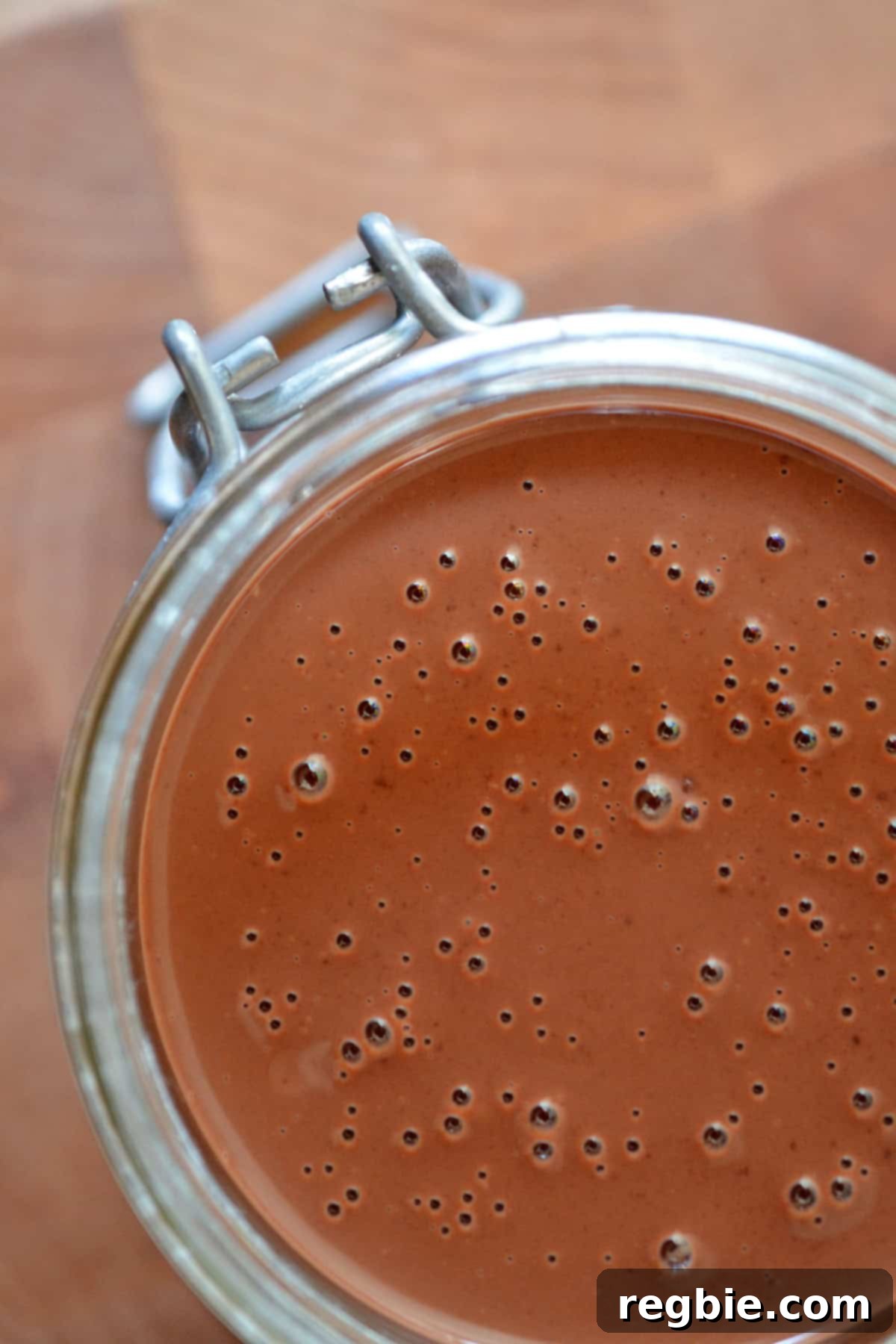 An overhead shot of glossy homemade chocolate ganache resting in a clear glass container, ready to be drizzled.