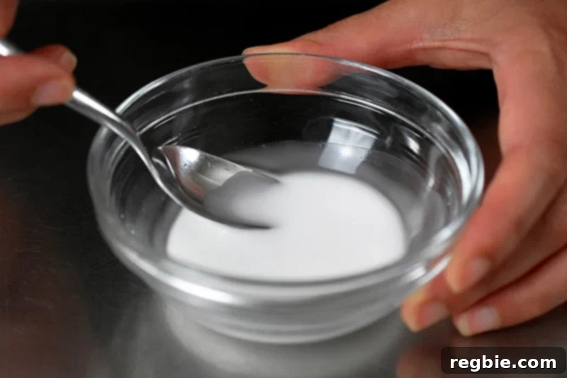 A small glass bowl neatly filled with a mixture of arrowroot starch and water, stirred smooth with a spoon, poised as a ready-to-use thickening slurry.