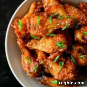 An overhead shot of a bowl filled with Asian Sticky Wings topped with sesame seeds and sliced scallions.