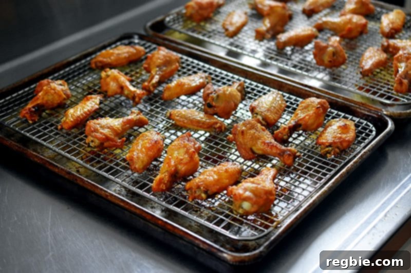 Two trays of golden-brown, crispy oven-baked chicken wings resting on wire racks on a kitchen counter, showcasing their perfect texture and even browning.