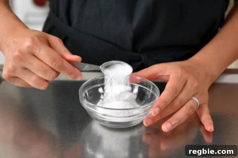 Illustrates the precise process of adding individual ingredients for grain-free and paleo baking powder into a small bowl, meticulously prepared for thorough mixing.