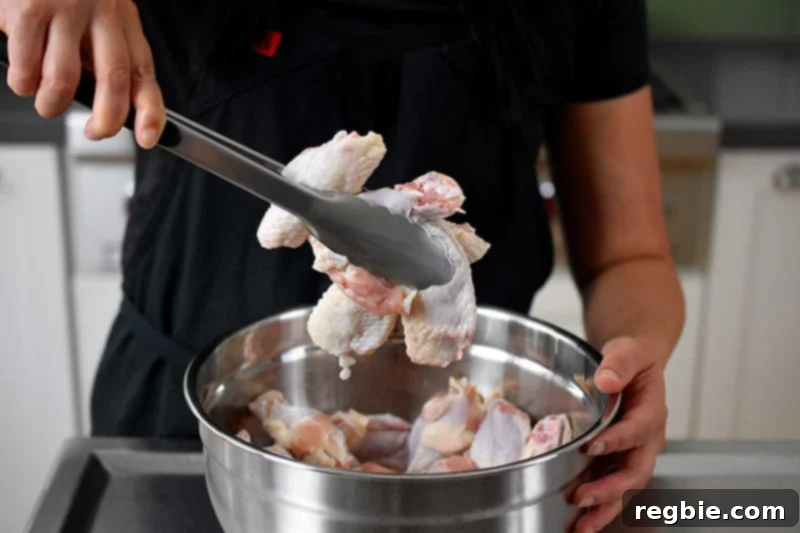 A pair of tongs is expertly used to toss chicken wings, ensuring they are thoroughly coated in the grain-free paleo baking powder mixture within a spacious mixing bowl.