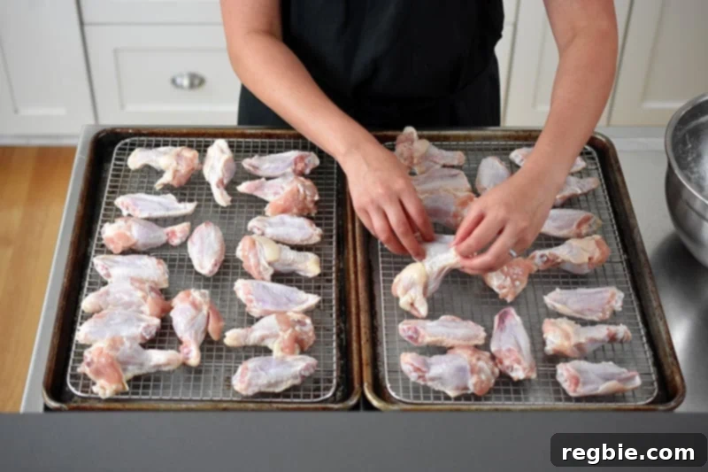 Demonstrates the careful arrangement of chicken wings in a single, uncrowded layer on wire racks, which are perfectly set within two rimmed baking sheets for even cooking.
