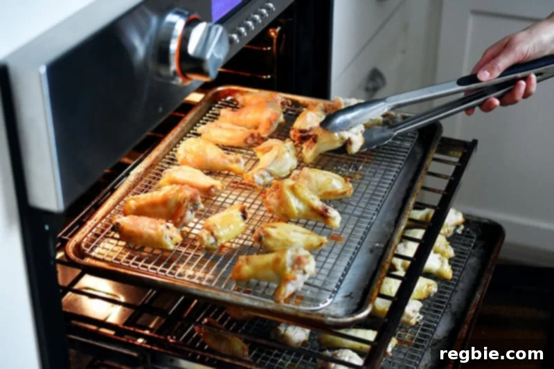 Someone skillfully using tongs to carefully flip individual chicken wings before rotating the trays in the oven, ensuring optimal crispiness and even cooking.