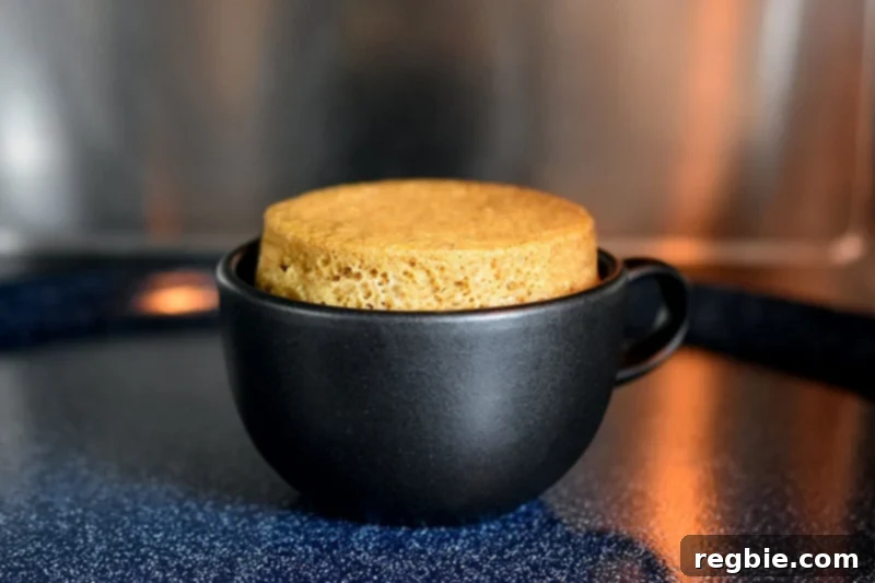 Quick Paleo Gluten-Free Pumpkin Mug Cake 8 A pumpkin mug cake that is golden brown inside a black coffee mug.