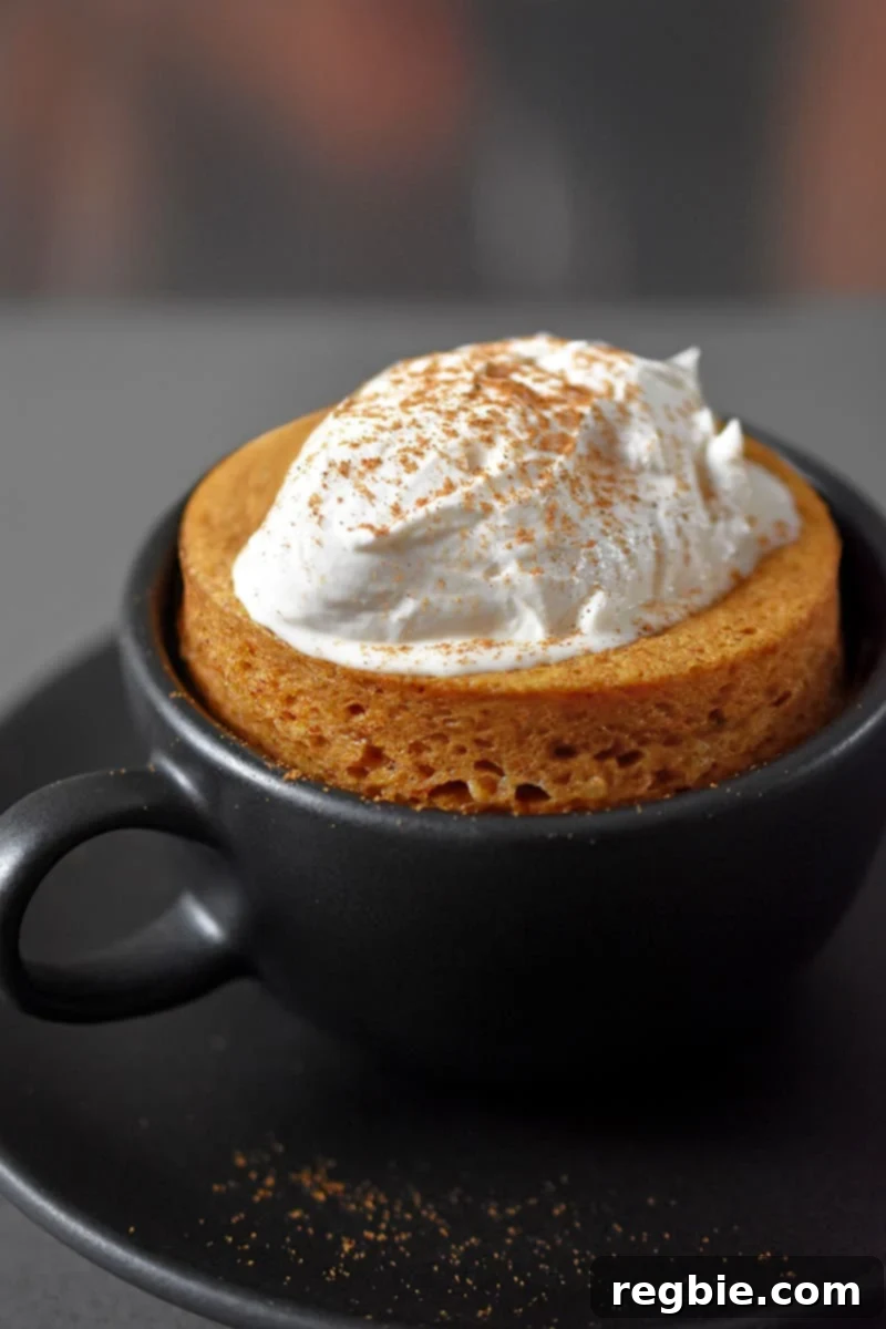 Quick Paleo Gluten-Free Pumpkin Mug Cake 9 A black coffee mug filled with paleo and gluten-free pumpkin mug cake cooked in the microwave.The cake is topped with whipped coconut cream and dusted with pumpkin spice blend.