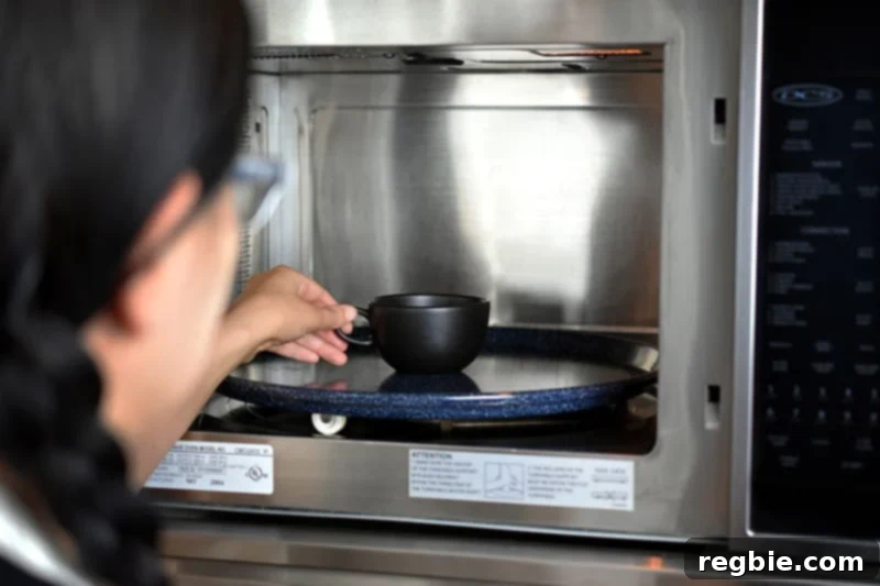 Paleo Black Sesame Mug Cake Indulgence 8 A brunette woman with glasses carefully placing a black tea cup filled with mug cake batter into the center of a microwave.