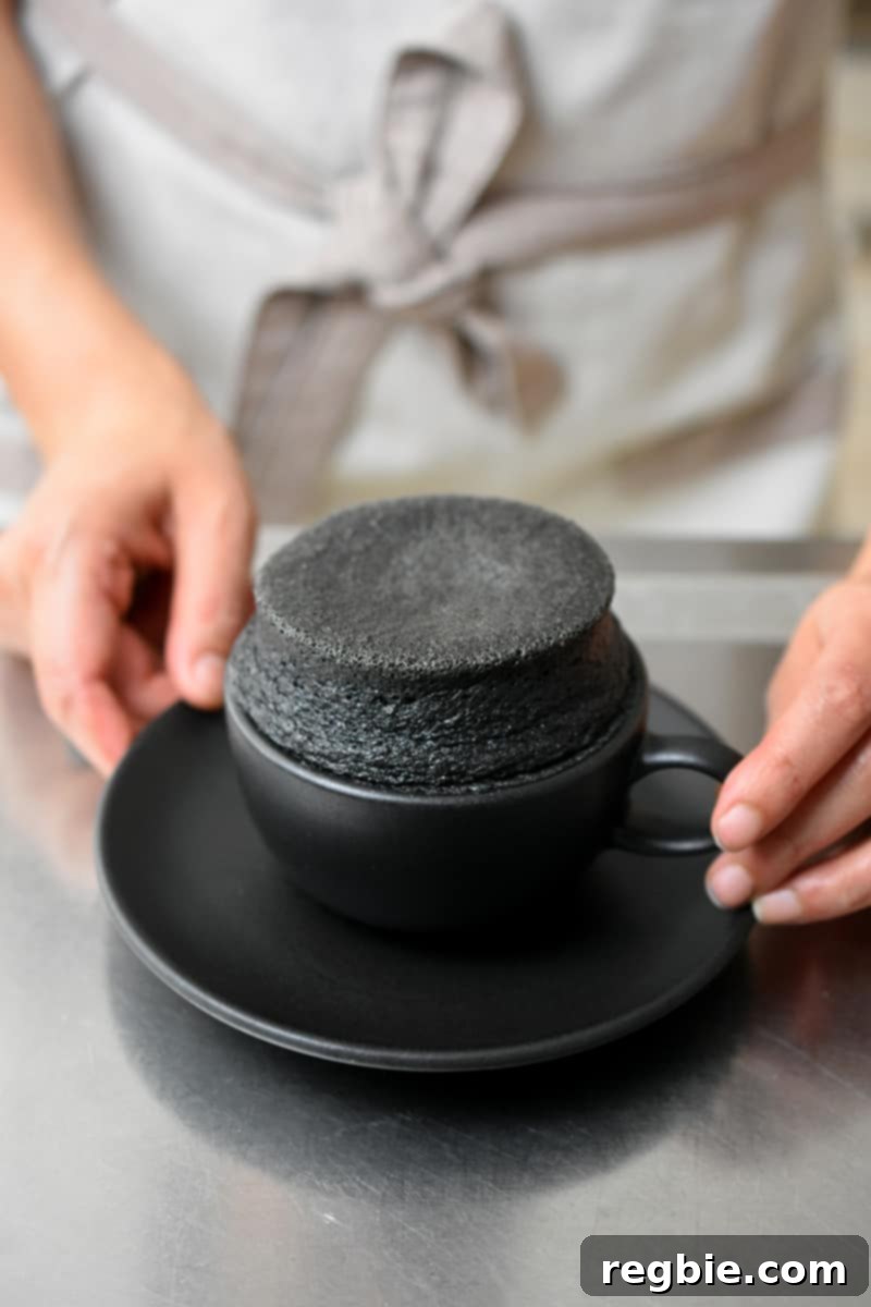 Paleo Black Sesame Mug Cake Indulgence 10 Two hands holding a black tea cup filled with a perfectly puffed-up, gluten-free and paleo black sesame mug cake, showcasing its inviting texture.
