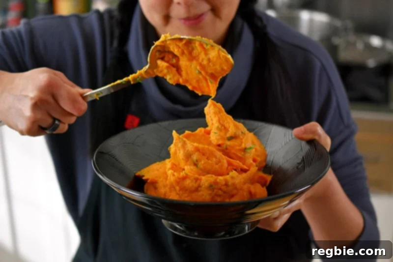 Scooping up Instant Pot Mashed Sweet Potatoes into a black bowl.