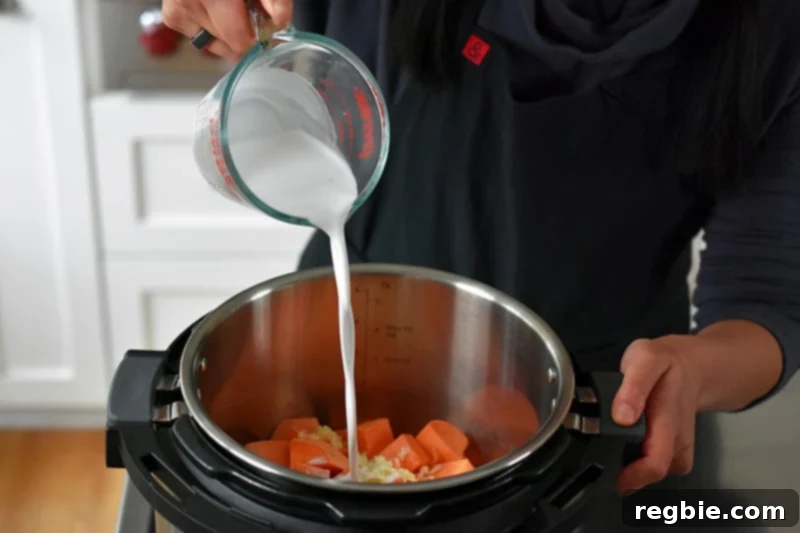 Pouring coconut milk into an Instant Pot filled with cubed sweet potatoes and minced garlic.