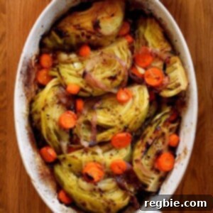 An overhead shot of the world's best braised green cabbage, carrot coins, and sliced onions in an oval casserole pan. Two hands are holding the handles with towels, suggesting it's hot and ready to serve.