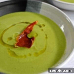 A closeup shot of vibrant green pea soup with crispy prosciutto on top, ready to be served.