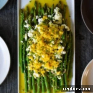 An overhead shot of a rectangular plate filled with Asparagus Mimosa, cooked asparagus tossed with a lemon vinaigrette and topped with chopped hard boiled eggs and chives. It’s a beautifully presented dish.