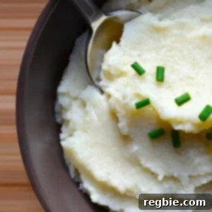 An overhead shot of a bowl filled with fluffy, garlicky cauliflower mashed potatoes, garnished with fresh herbs.